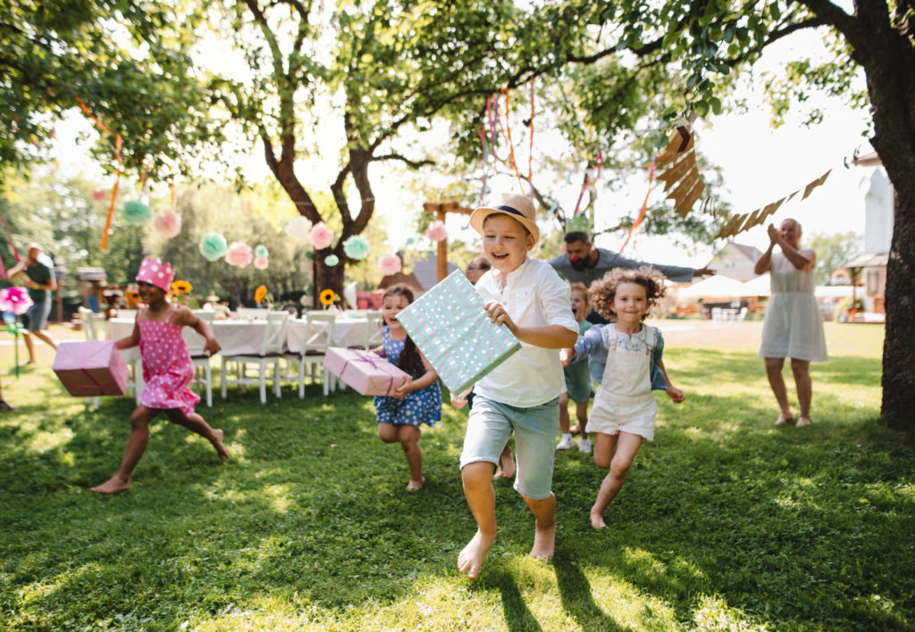 Small children ruunning with present outdoors in garden on birthday party.