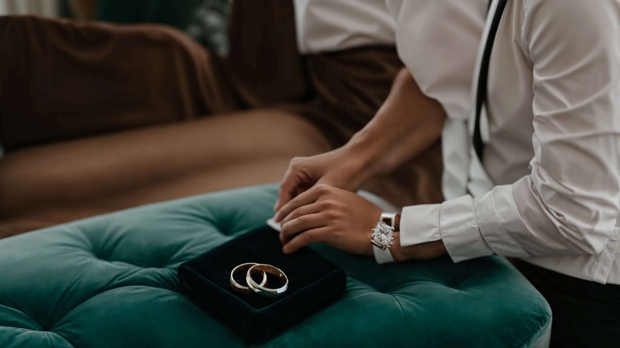 a groom gently places a sleek wedding band onto a velvet cushion amidst wedding preparations.